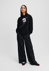 Haut à capuche noir avec un graphique de cartoon, associé à un pantalon large noir et des baskets noires. Design minimaliste, style décontracté.