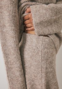 Beige gebreide sweater met een geribbelde textuur en brede mouwen, gedragen over bijpassende gebreide hoge taille broek, met een zachte, comfortabele stof.
