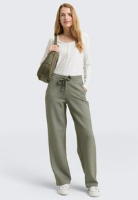 Casual outfit bestaande uit een wit shirt met lange mouwen en losse, olijfgroene sweatpants met een elastische tailleband en trekkoord; gecombineerd met een groene tas.