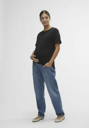 Svart kortärmad t-shirt i kombination med ljusblå, löst sittande jeans. Modellen står i en avslappnad pose och visar upp en avslappnad stil. Platta skor fulländar looken.