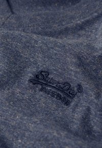 Maglietta in cotone blu navy con una texture morbida, caratterizzata da un logo ricamato in blu scuro sul lato inferiore destro.