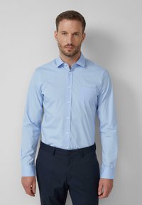 Helleblaue Langarmbluse mit kleinem Pünktchenmuster, Knopfleiste und einer Brusttasche. Der Stoff hat eine glatte Textur.