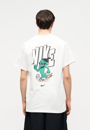 Person wearing white Nike T-shirt with large "NIKE" text and cartoon character running with flaming shoes on the back.