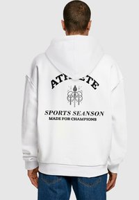 Biela mikina s kapucňou a voľným strihom, na chrbte s čiernym textom: "ATHLETE," "SPORTS SEASON," a "MADE FOR CHAMPIONS."