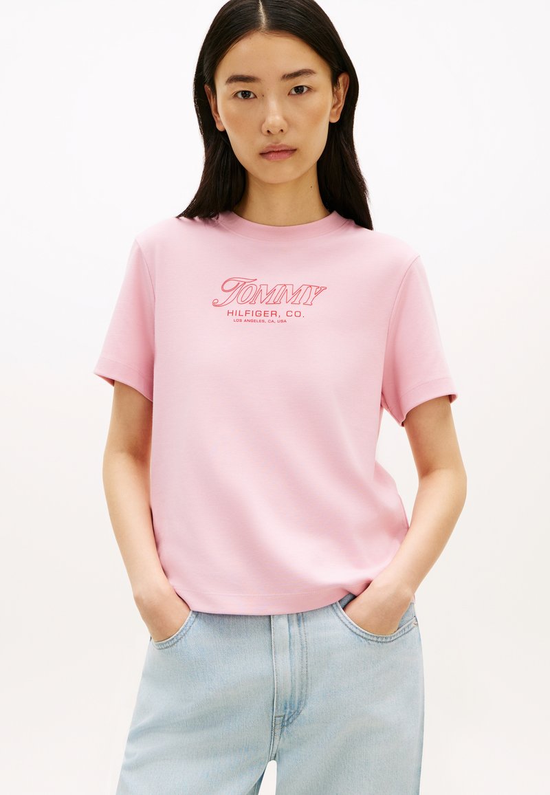 Ροζ βαμβακερό t-shirt με κοντά μανίκια και λαιμόκοψη τύπου crew, με ένα στυλιζαρισμένο λευκό και κόκκινο λογότυπο "TOMMY HILFIGER" στο στήθος.