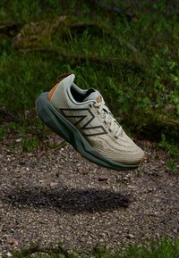 Lett løpesko i beige med teksturert overdel, grønn såle og oransje detaljer. Har en pustende design og snøring.