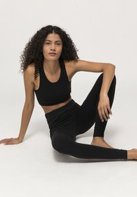 Zwarte sportieve crop top en leggings, aansluitend ontwerp, zachte textuur en gladde stof. Model poseert zittend met een ontspannen houding op een lichte achtergrond.