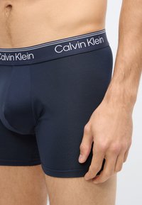 Cuecas boxer Calvin Klein azul-marinho com tecido macio e elástico; cintura elástica com logo branco e detalhe de dupla listra.