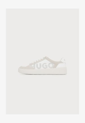 Zapatilla blanca y beige de perfil bajo con detalles perforados en el lateral que forman la palabra "HUGO" y una suela blanca gruesa sobre un fondo liso.