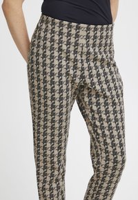 Pantaloni con un tessuto testurizzato e un motivo pied-de-poule nero e beige. Vestibilità dritta, vita alta, materiale elastico.
