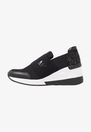 Zapatillas deportivas negras con parte superior de malla, tirante elástico y talón texturizado negro. Acentos de suela blanca y herrajes negros brillantes.