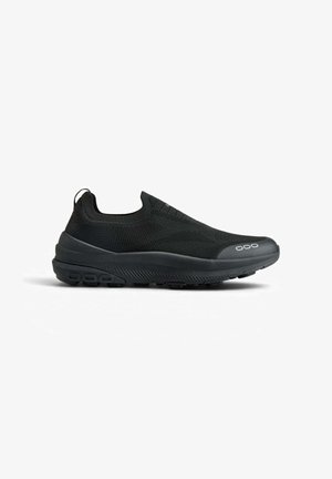 Schwarzer Slip-on-Sportschuh mit gestricktem Obermaterial, gepolsterter Sohle und kleinem reflektierendem Detail an der Spitze, auf weißem Hintergrund positioniert.
