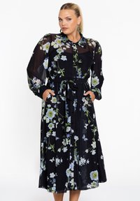 Schwarzes Blumenkleid mit langen transparenten Ärmeln, Knopfleiste und taillierter Taille. Mit grünen und blauen Blumenmustern sowie seitlichen Taschen.