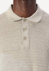 Beige kudumustriga polo särk, millel on tavaline krae, kolm pruuni nuppu ja lühikesed varrukad.