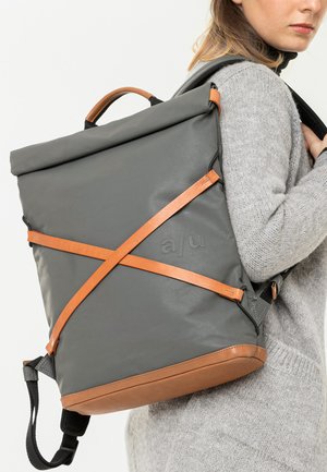 Grau roll-top Rucksack mit braunen Lederakzenten und Crossbody-Trägern. Verfügt über eine glatte Textur und gepolsterte Schulterriemen.