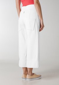 Pantaloni bianchi a gamba larga con elastiche in vita e due tasche posteriori. Tessuto in cotone liscio con lunghezza cropped. Abbinati a scarpe chiare.