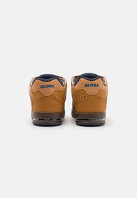 Brown leather sneakers with a textured finish, featuring a navy blue padded collar and visible cushioning in the sole. Brand logo on the back.