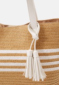 Přírodní pletená slámová taška s bílými pruhovanými akcenty. Obsahuje bílý kožený popruh a dekorativní bílé třásně.