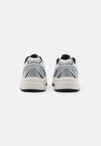 Scarpe sportive grigio chiaro con tomaia in rete, dettagli neri e suola bianca. Presentano un design elegante e elementi testurizzati sui lati.