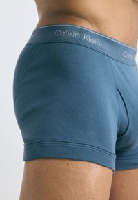 Boxerii pentru bărbați, dintr-un material teal, cu un design ajustat. Prezintă un mărgină elastică moale, cu brandul "Calvin Klein".