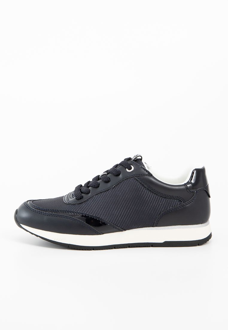 Schwarz-weißer Sneaker mit strukturierten Seitenpaneelen, Schnürverschluss und flachem Profil, von der Außenseite auf einem weißen Hintergrund gezeigt.