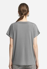 Kortärmad grå topp för kvinnor med avslappnad passform, mjuk textur och rundad halsringning, med en något krökt fåll.