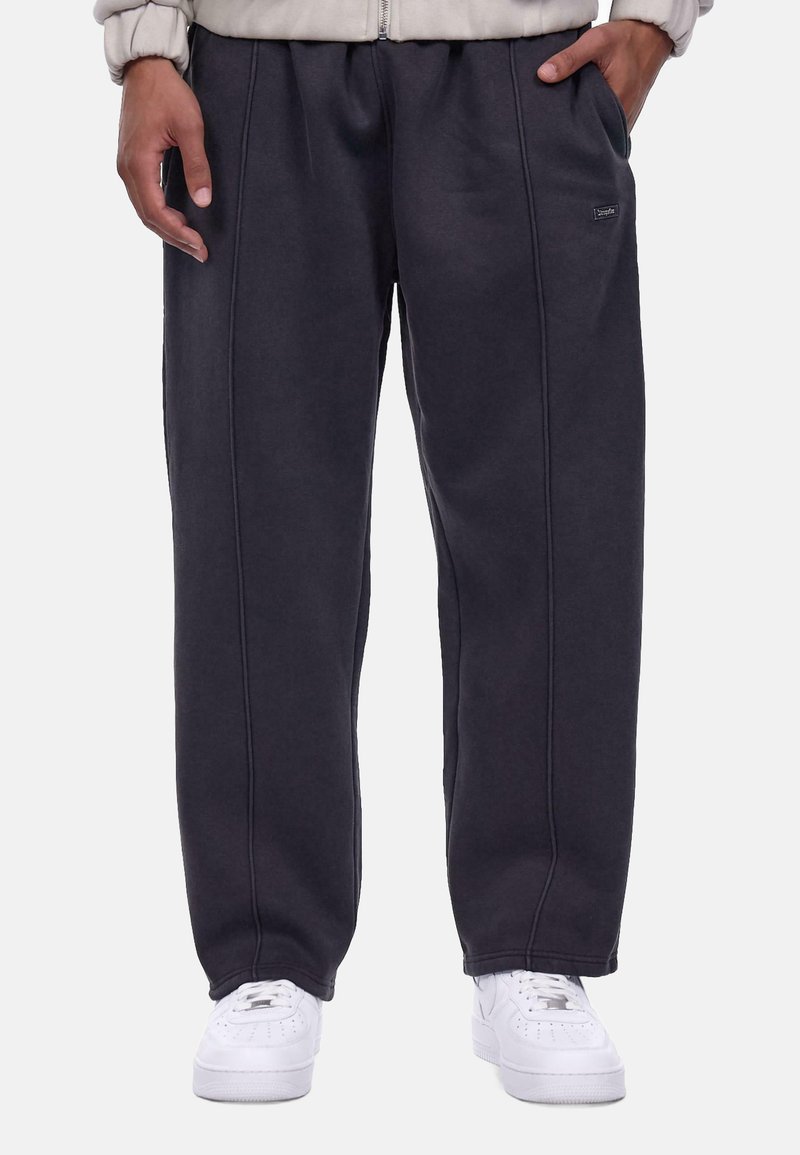 Kulkulsorte sweatpants lavet af blødt stof, med sidelommer, elastisk talje og kontrasterende syninger. Båret med hvide sneakers.