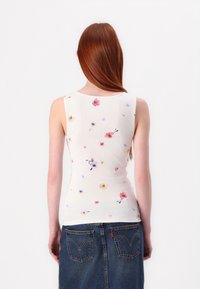 Top sans manches blanc avec une texture côtelée, présentant un imprimé floral coloré. Associé à une jupe en denim, vue de dos.