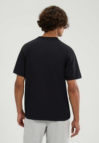 Czarny t-shirt z krótkim rękawem, wykonany z bawełny, o luźnym kroju, z okrągłym dekoltem i minimalistycznym wzornictwem. Brak widocznych logo lub wzorów.