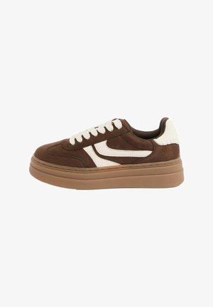 Barna velúr sportcipő fehér oldalsávval, fehér fűzőkkel, fehér sarokpárnával és vastag világosbarna talppal.