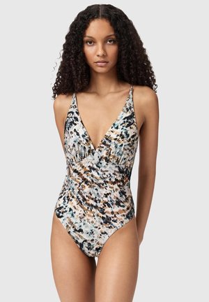 Vrouw met krullend haar die een mouwloos, diep V-hals badpak met een multicolor abstract patroon draagt.