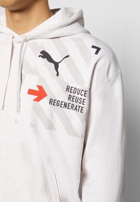 Bílá mikina s kapucí vyrobená z bavlněné směsi, s grafickým designem, který zahrnuje logo černé kočky, červenou šipku a text "REDUCE REUSE REGENERATE."