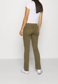 Zelené kalhoty rovného střihu z bavlněné směsi. Mají dvě zadní kapsy a středně vysoký pas, kombinované s bílými teniskami.