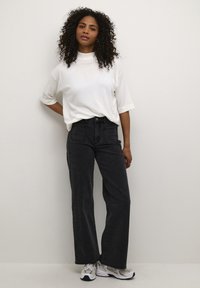 White short-sleeve top and high-waisted black jeans, featuring pockets and a relaxed fit. Worn with gray and black sneakers.