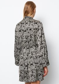 Schwarzes Kleid mit einem weißen Blattmuster, ausgestattet mit langen Ärmeln, einer taillierten Taille und einem plissierten Rock. Leichte Stoffqualität mit glatter Textur.
