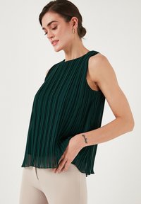 Grøn, plisseret ærmeløs top med høj hals, let stof og en svævende design, der har en subtil gennemsigtighed og en afslappet pasform.