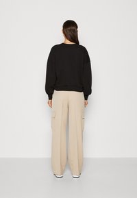 Sudadera negra de gran tamaño con mangas abullonadas, combinada con pantalones cargo beige de cintura alta que cuentan con bolsillos laterales y un ajuste relajado.