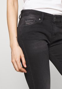 Vaqueros de denim negro con ajuste slim, diseño de cinco bolsillos y detalles de costura sutil. Textura suave con un ligero brillo.