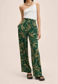 Green wide-leg pants with a gold leaf pattern; lightweight fabric. Paired with a one-shoulder white top and black platform sandals.