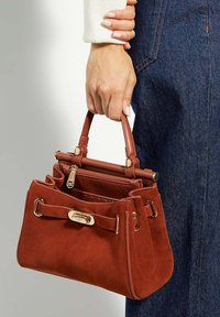 Burnt orange suede handbag with gold hardware, top handles, and an interior zip pocket. The bag features a structured shape and detachable accents.