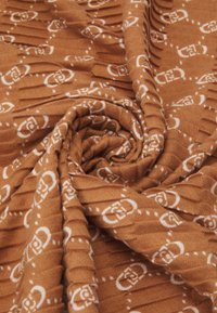 Tissu brun texturé avec un motif blanc, présentant des crêtes en relief et une disposition en spirale, créant une apparence douce et tactile.