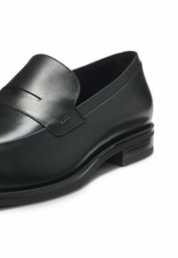 Mocassins en cuir noir avec une finition lisse, présentant un design piqué et un détail découpé subtil sur le dessus. Talon bloc bas.