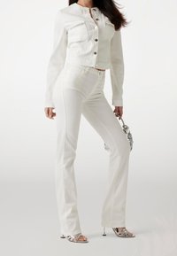 Valkoinen farkkutakki, jossa on etutaskut, pyöreä kaula-aukko ja hopeiset napit. Kapeat valkoiset farkut, joissa liehuvat lahkeet. Asusteina hopeinen käsilaukku ja sandaalit.