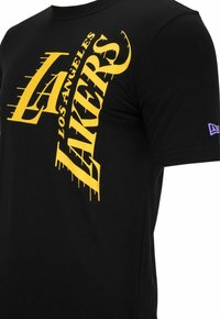 Camiseta de algodón negra con un gráfico audaz en amarillo que dice "Los Angeles Lakers" con efecto de salpicadura, mangas cortas y un pequeño logo púrpura en el costado.