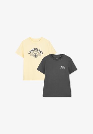 Twee T-shirts: één lichtgeel met een marineblauw logo, de ander donkergrijs met een kleiner logo. Beide zijn kortärmelig en gemaakt van katoen.