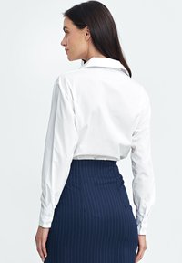 Biała, długosleeve'owa koszula z gładkiego materiału, z klasycznym kołnierzykiem i mankietami na guziki, połączona z granatową spódnicą w paski o wysokim stanie.