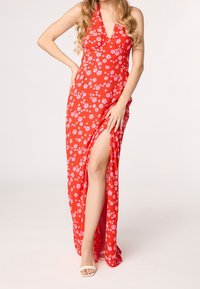Červené maxi šaty s květinovým motivem, které mají zavazování za krkem, vysoký rozparek a lehký materiál s růžovými květinovými vzory. Hladká textura a splývavý design.