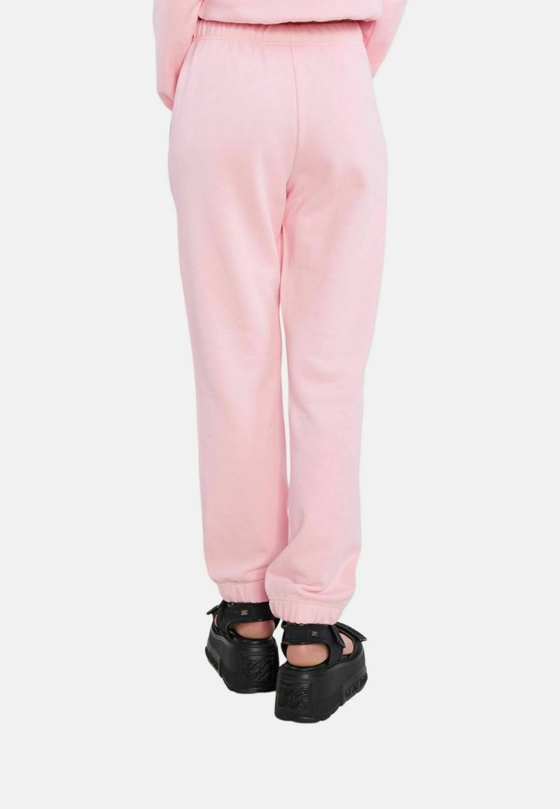 Rosa Jogginghose mit elastischem Bund und Bündchen, kombiniert mit schwarzen klobigen Sandalen mit Riemen. Einfache und weiche Stofftextur.