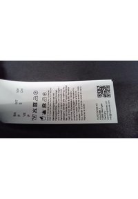 Étiquette d'entretien du linge avec symboles de lavage, instructions d'entretien multilingues, code QR et coordonnées de Hugo Boss sur fond noir.