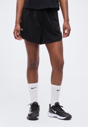 Person iført sorte atletik mesh shorts, hvide Nike crew sokker og sorte Nike sneakers, stående mod en ensfarvet hvid baggrund.
